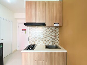 A compact kitchen with wooden cabinets, a tiled backsplash, and a stainless steel sink.