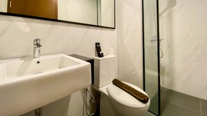 Une salle de bain avec un lavabo blanc, des toilettes, une douche en verre et un miroir au-dessus du lavabo.