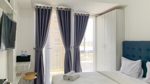 A hotel room with a bed, a TV mounted on the wall, a small bar area, and a window with curtains. - Luxurious Studio At 7Th Floor Tokyo Riverside Pik 2 Apartment (Teluknaga)