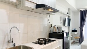 A modern kitchen with a stainless steel sink, a gas stove, and a built-in oven. There is a black countertop and white cabinetry. A kettle and a toaster are on the counter. - Luxurious Studio At 7Th Floor Tokyo Riverside Pik 2 Apartment (Teluknaga)