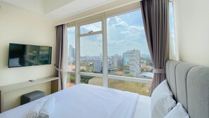 A hotel room with a large window, a flat-screen TV, a neatly made bed, and a small seating area. - Nice And Minimalist 2Br At Menteng Park Apartment (Jakarta)