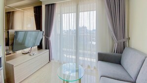 A modern living room with a flat-screen TV on a wooden console, a glass coffee table, a grey sofa, and large floor-to-ceiling windows with sheer curtains. - Nice And Minimalist 2Br At Menteng Park Apartment (Jakarta)