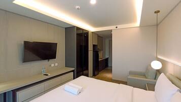 A hotel room with a bed, a TV mounted on the wall, a desk with a chair, and a small table with a lamp.