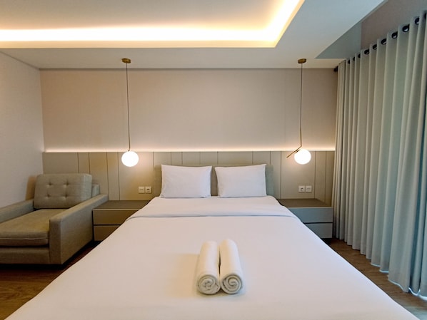 A modern hotel room with a large bed, two bedside tables, a sofa, and a view of the city through large windows.