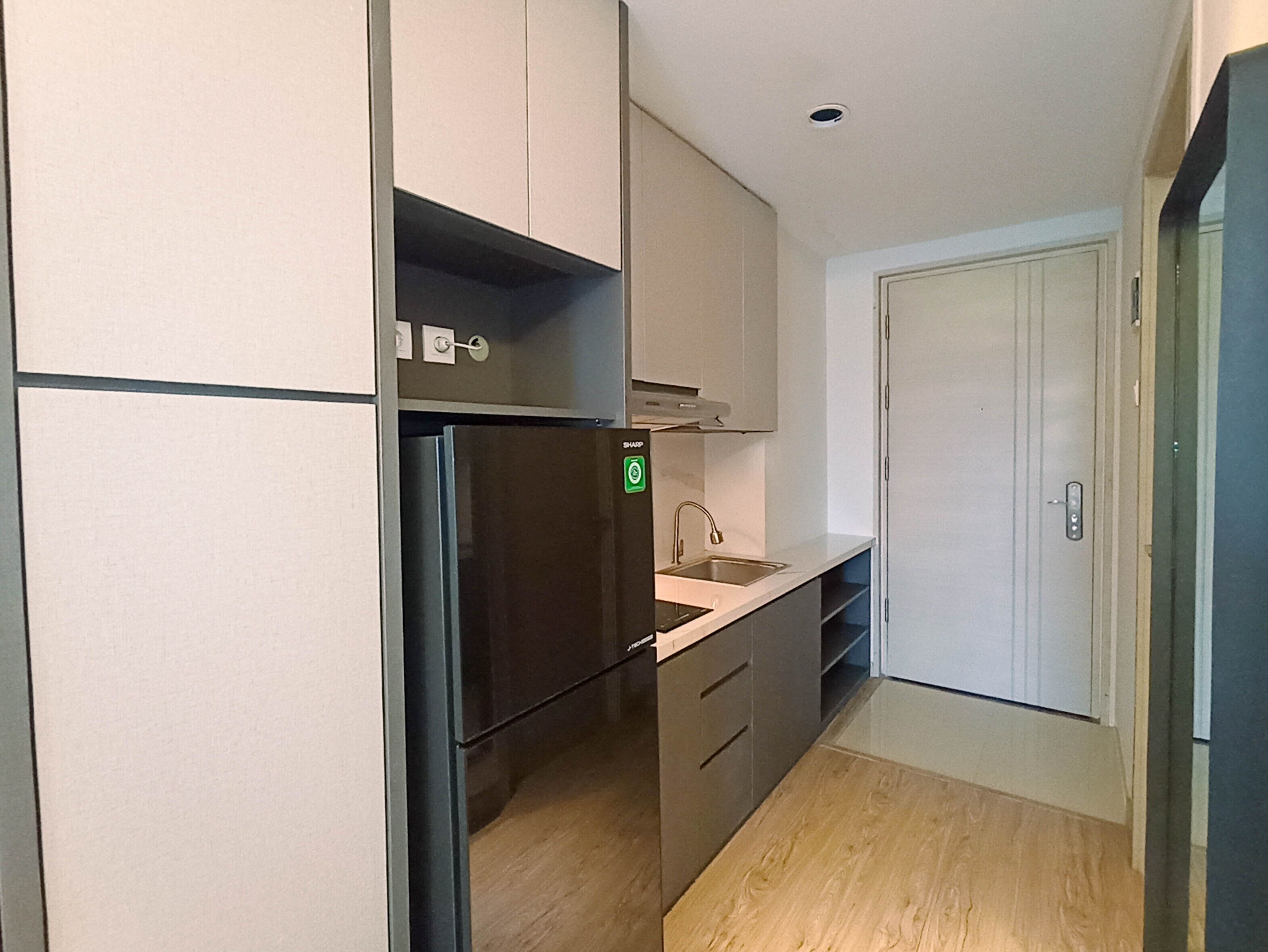 A compact kitchen with a built-in refrigerator, a sink, and a door leading to another room.
