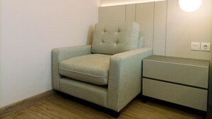 Una habitación pequeña y moderna con un sillón de color claro, una mesita de noche con cajones e iluminación empotrada en la pared.