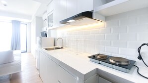 A modern kitchen with white cabinetry, a stainless steel sink, a built-in oven, and a black range hood. - New And Modern Studio At Daan Mogot City Apartment (Jakarta)