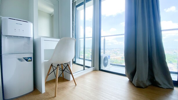 A modern room with a white desk, a white chair, a white air conditioning unit, and a large window with a view of a cityscape. - New And Modern Studio At Daan Mogot City Apartment (Jakarta)