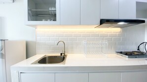 A modern kitchen with a stainless steel sink, a black range hood, and a white tiled backsplash. - New And Modern Studio At Daan Mogot City Apartment (Jakarta)