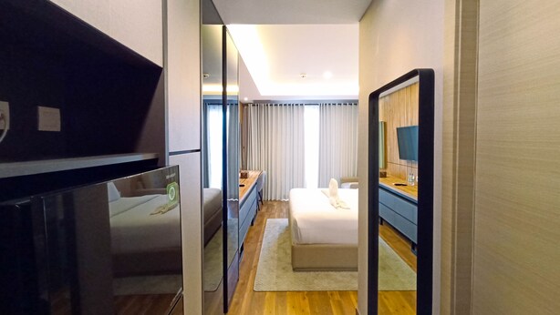 A hotel room with a bed, a desk, a mirror, and a television. - Cozy Studio Room At Mataram City Apartment (Ngaglik)
