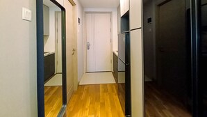 A narrow hallway with wooden flooring, white walls, and a white door at the end. - Cozy Studio Room At Mataram City Apartment (Ngaglik)
