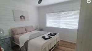 Quarto com cama, mesa de cabeceira e janela com persianas.