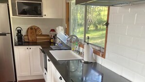 Uma cozinha com armários brancos, bancada preta, micro-ondas, fogão e janela com vista para o verde.