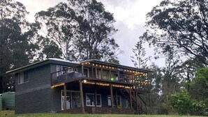 Uma casa de dois andares com varanda e alpendre, rodeada por árvores.