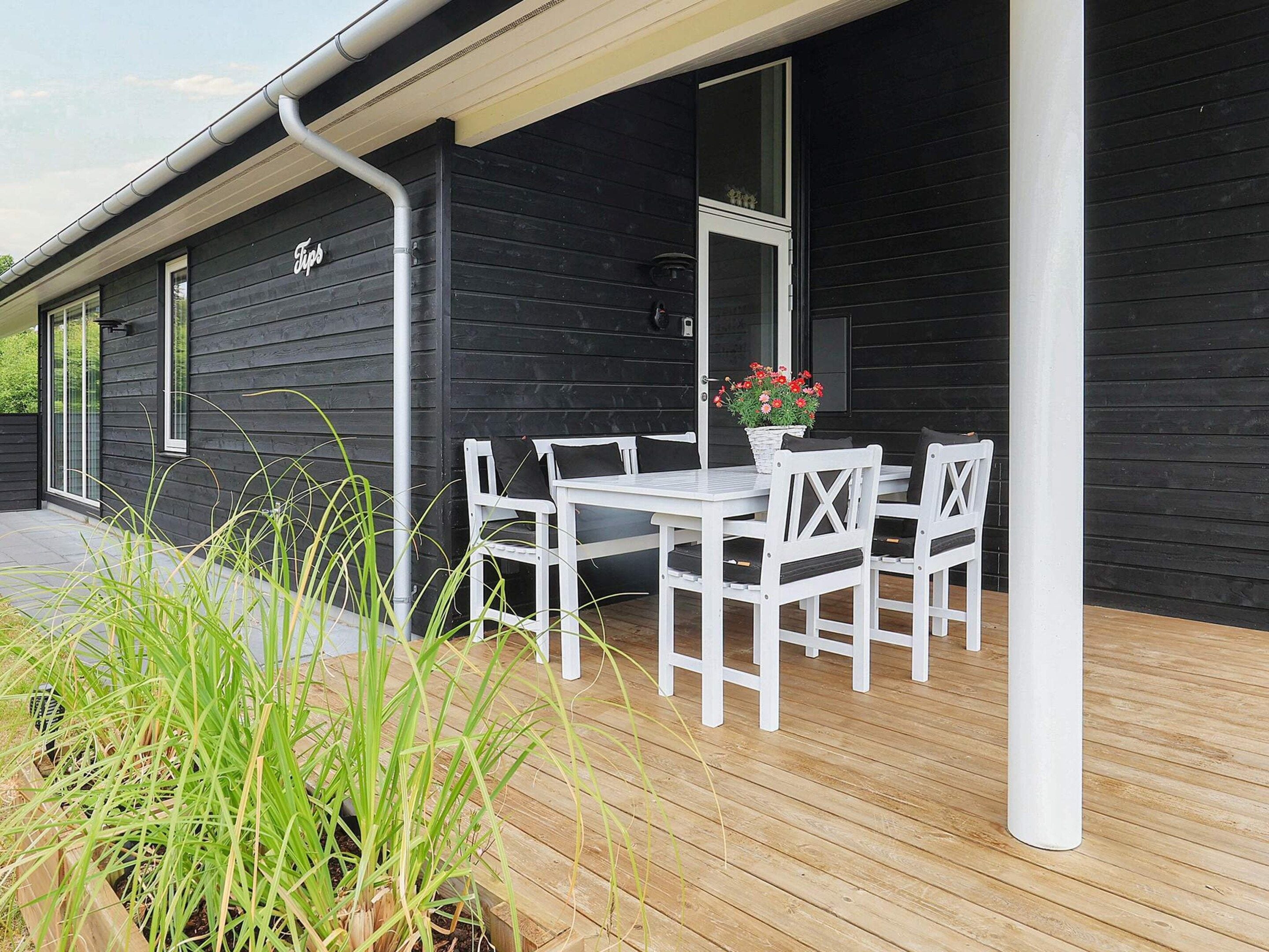 A black building with a white porch, a table with chairs, and a potted plant.