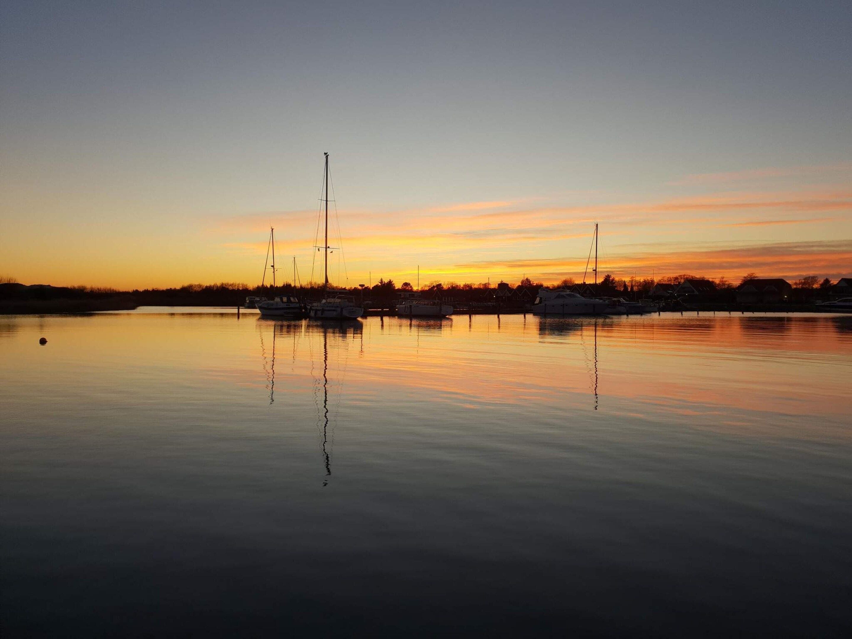 Rustig water waarop bootjes en een ondergaande zon weerspiegeld worden.
