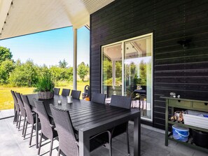 An outdoor patio with a long table and chairs, a grill, and a storage cabinet.