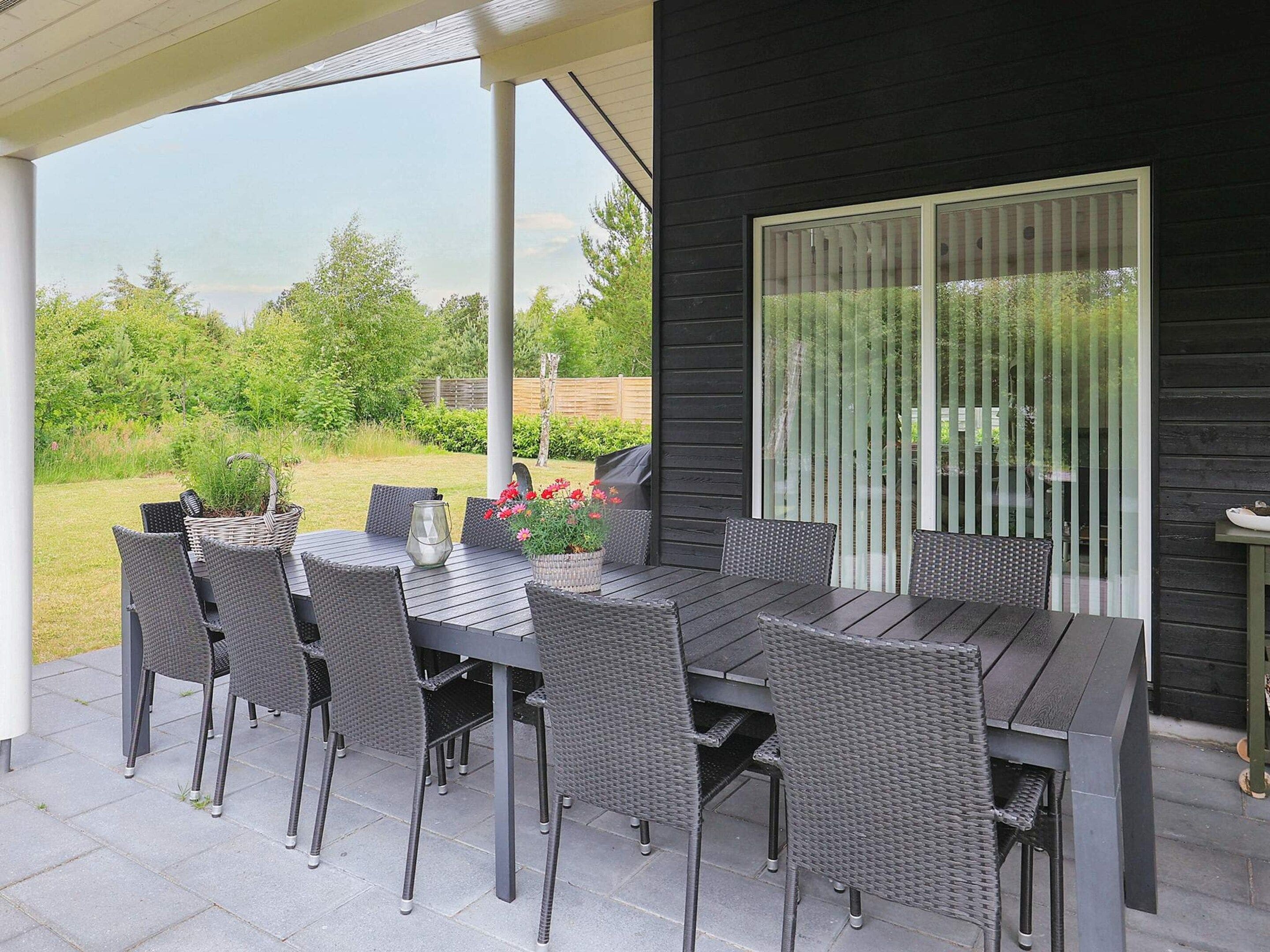An outdoor patio with a table and chairs, a grill, and a view of a garden.