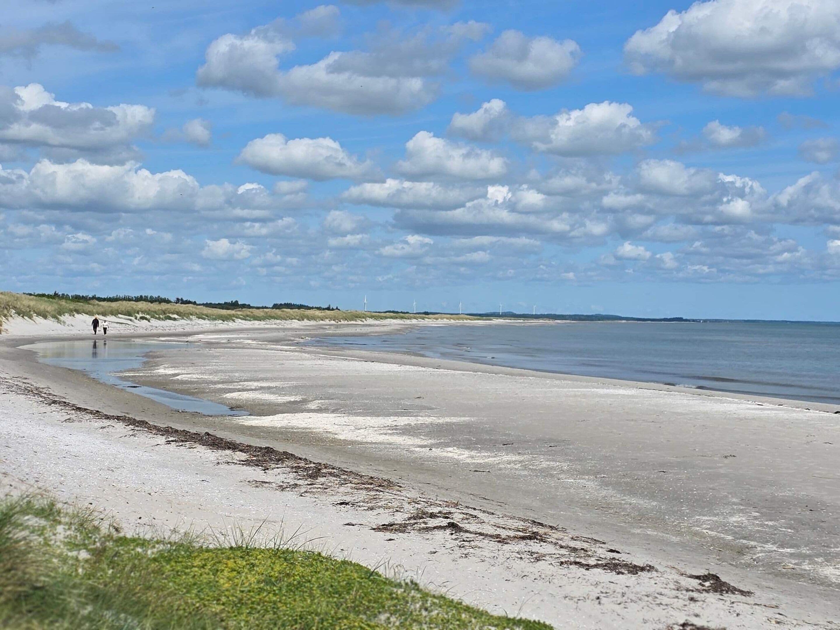 A beach with a wide sandy shore, a calm sea, and a clear sky with scattered clouds.