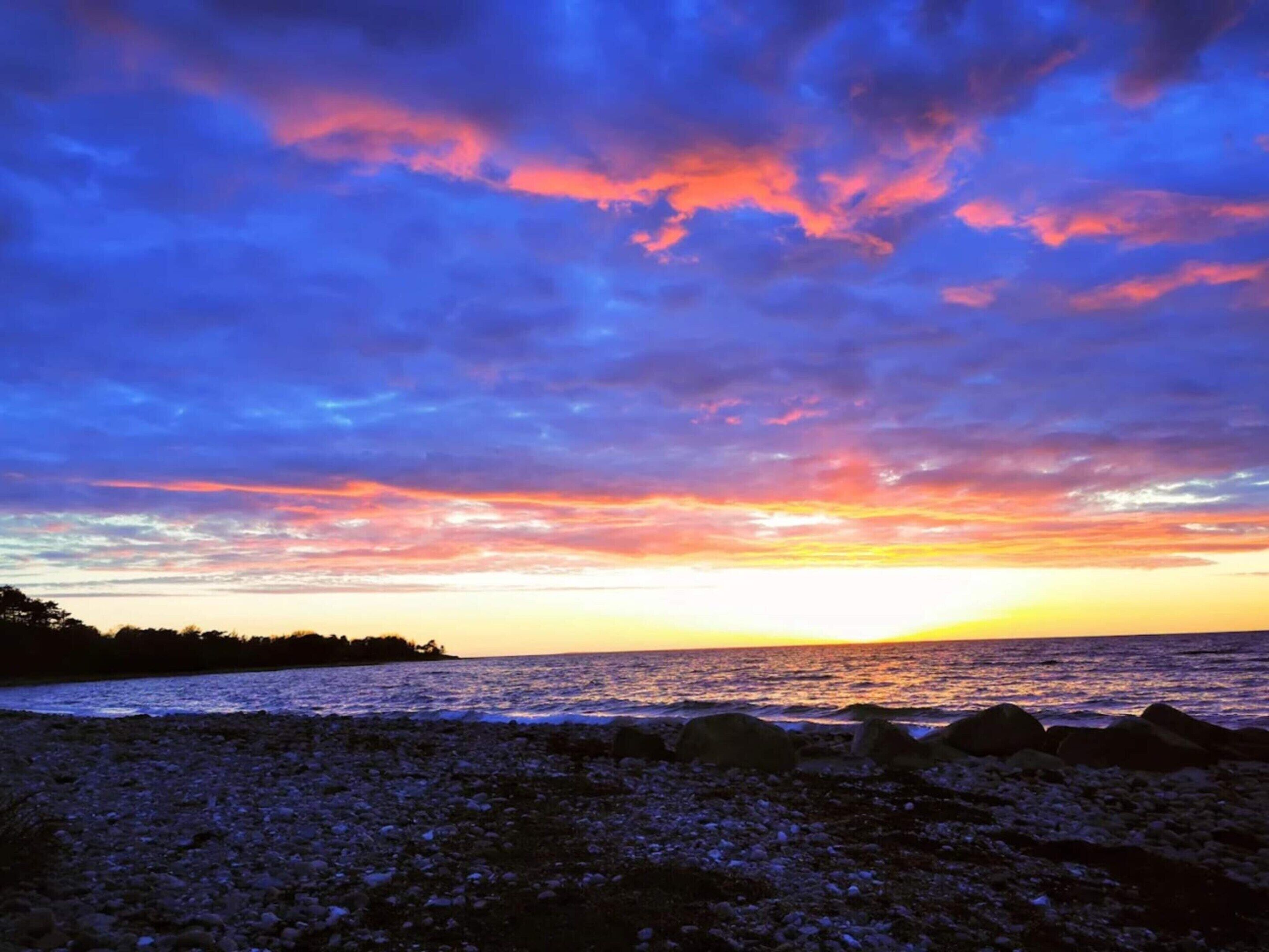 Ein Strand mit felsigem Vordergrund und einem Sonnenuntergang über dem Ozean.