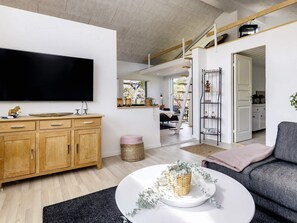 A modern living room with a large flat-screen TV, wooden cabinets, a grey sofa, and a staircase leading to an upper level.