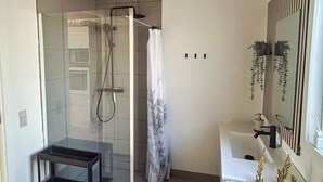 A modern bathroom with a glass-enclosed shower, a white sink, and a mirror with vertical stripes.