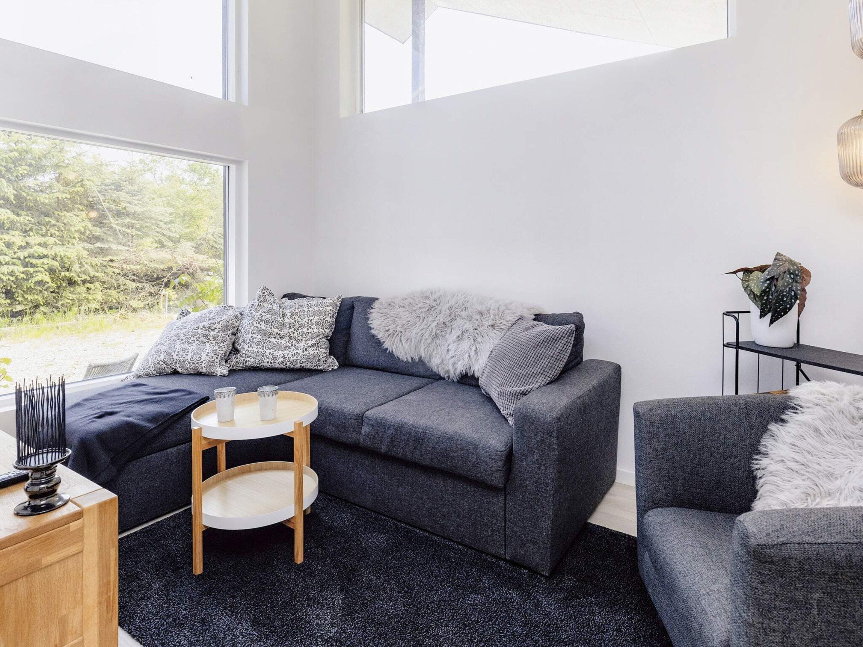 A modern living room with a grey sofa, a small round table, and a view of greenery outside.
