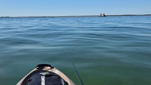 A calm body of water with a fishing rod and a boat in the foreground.