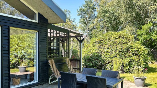 A patio with a table and chairs, a pergola, and a view of a garden.