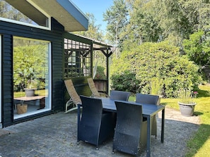 Um pátio com mesa e cadeiras, uma pérgula e vista para um jardim.