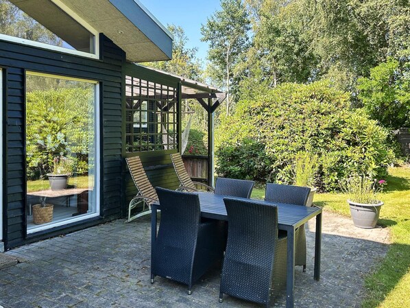 Une terrasse avec une table et des chaises, une pergola et une vue sur un jardin.