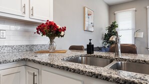 A modern kitchen with white cabinets, granite countertops, a stainless steel sink, and a hanging pendant light. - Historic CozySuites 4BR 2BA  (Louisville)