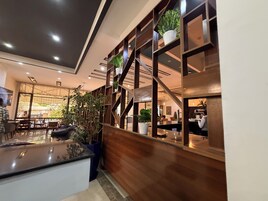 Un interior moderno con un mostrador de recepción de madera, plantas en macetas y vistas al comedor.