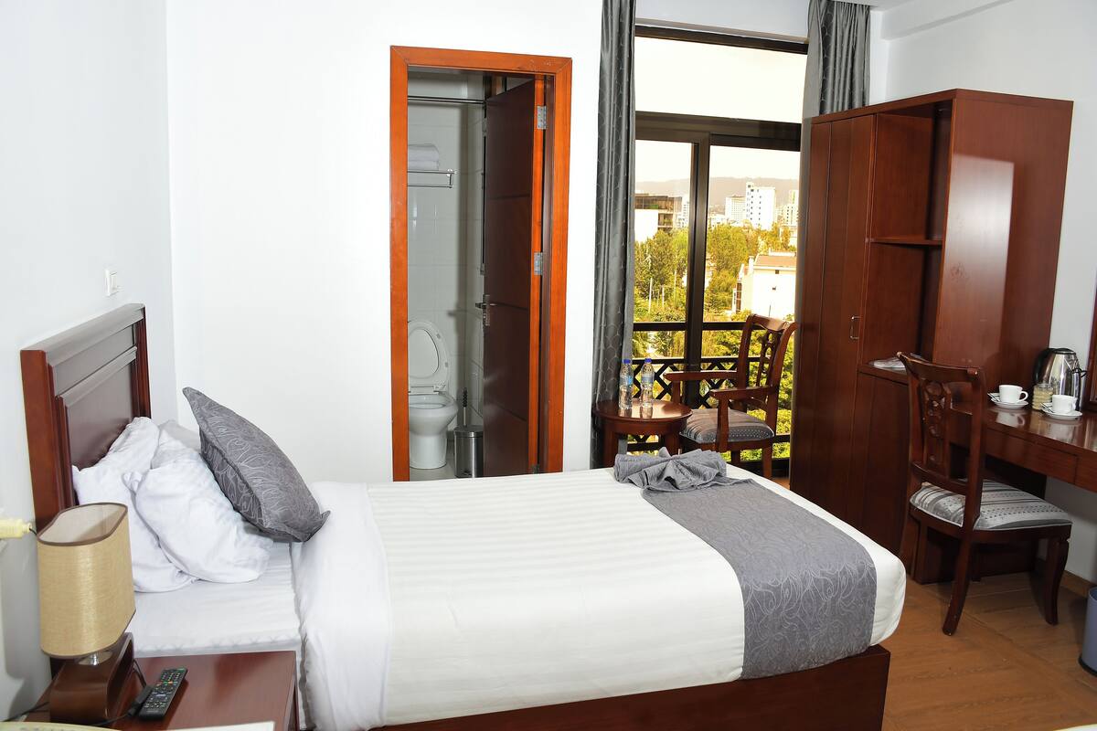 A hotel room with a bed, a desk, a chair, a balcony with a view, and a wardrobe.
