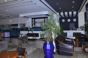 Un moderno vestíbulo de hotel con una zona de bar, arreglos de asientos y un gran jarrón azul con una planta.