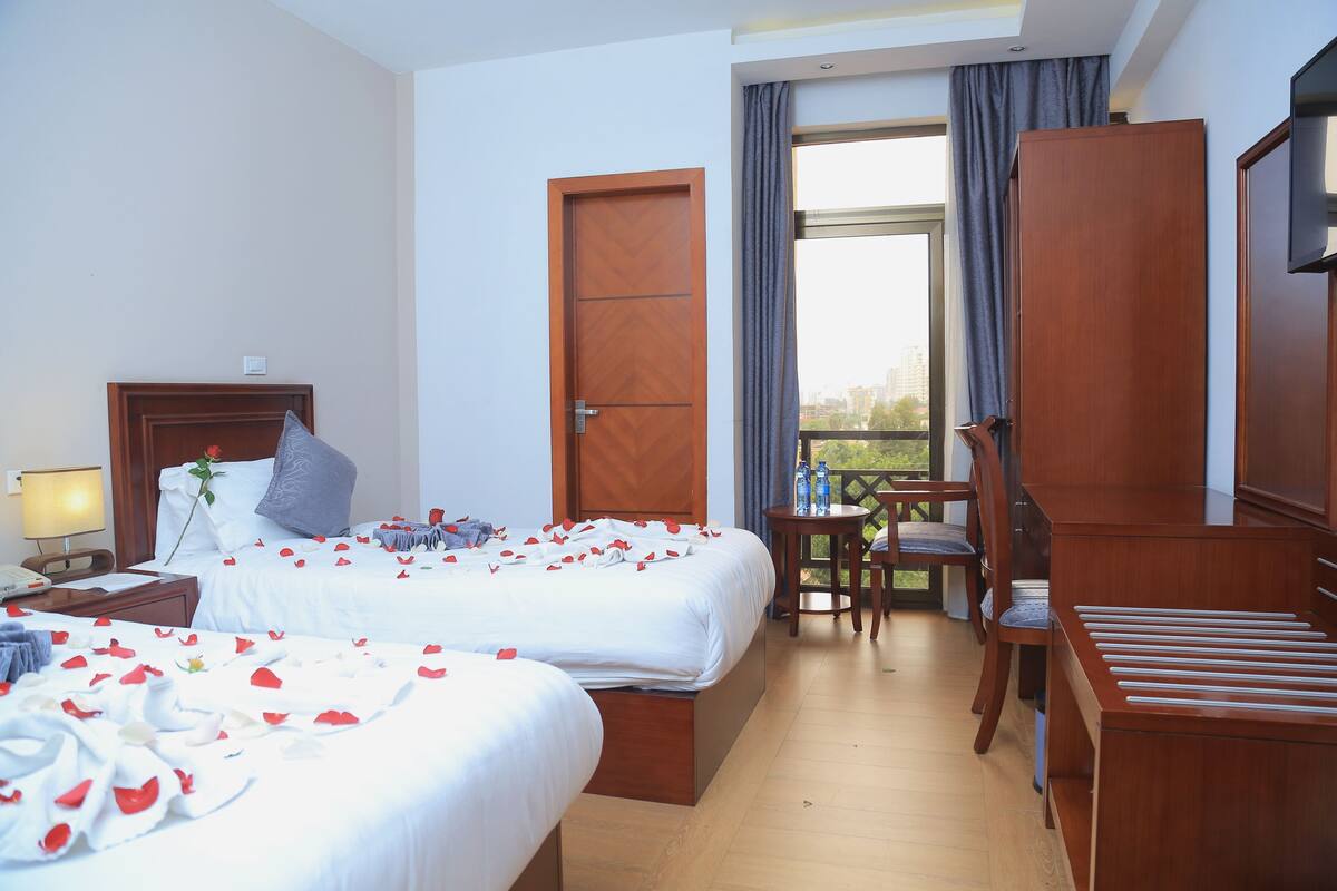 A hotel room with two beds, a desk, a chair, a wardrobe, and a balcony with a view.