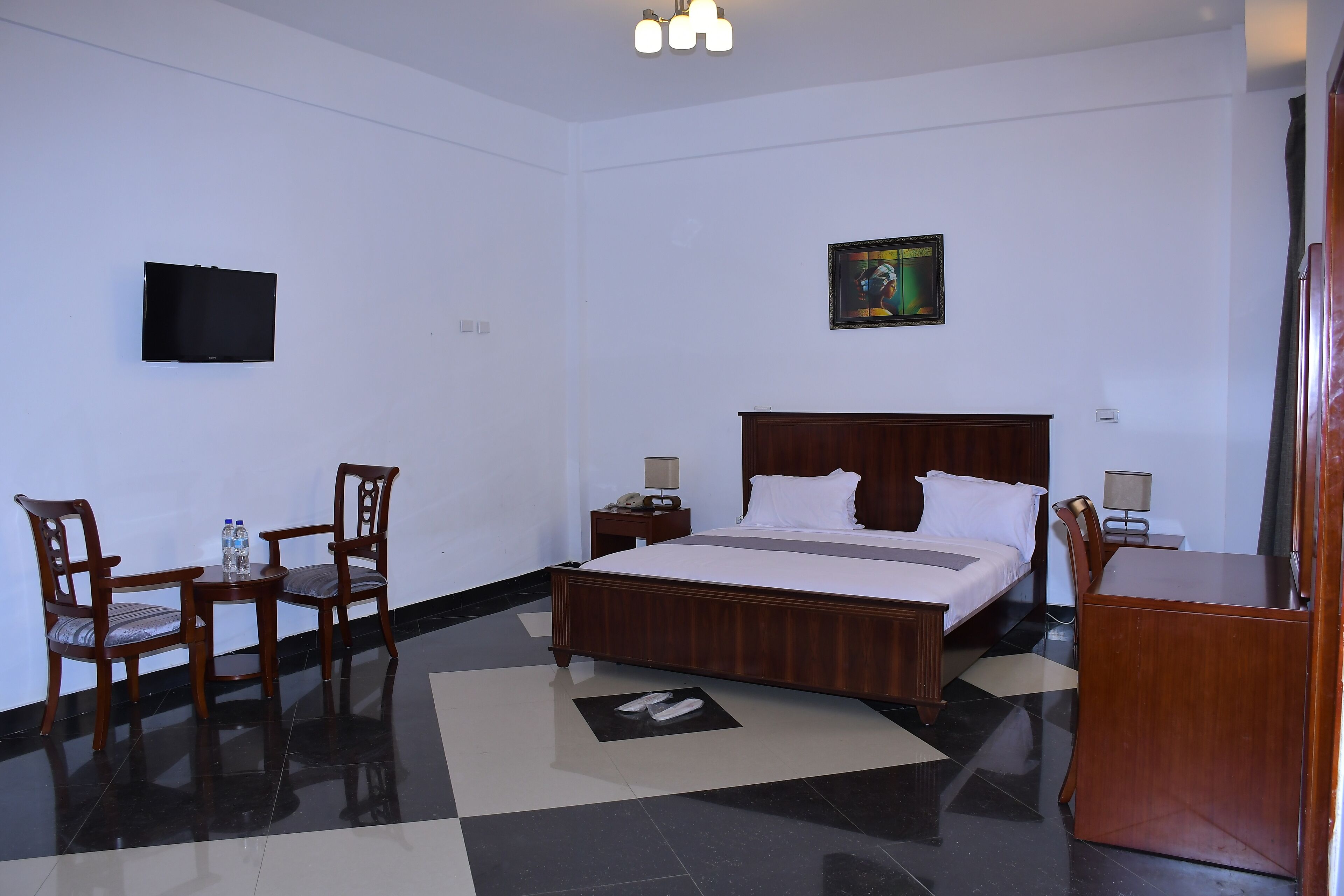 Habitación de hotel con cama, dos sillas, una mesita, televisión y un cuadro en la pared.