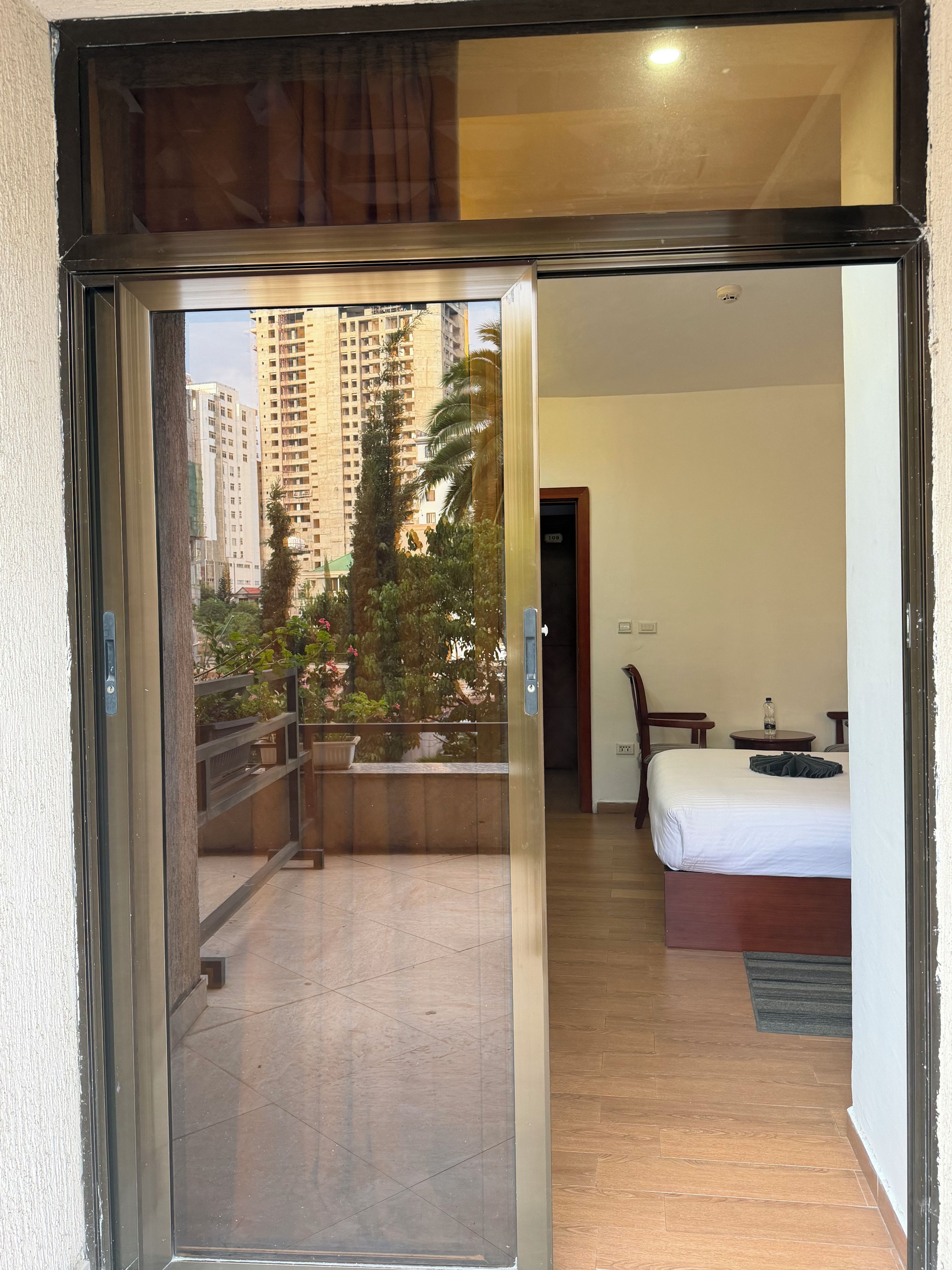 Una habitación de hotel con balcón, cama, escritorio y vista a edificios altos.