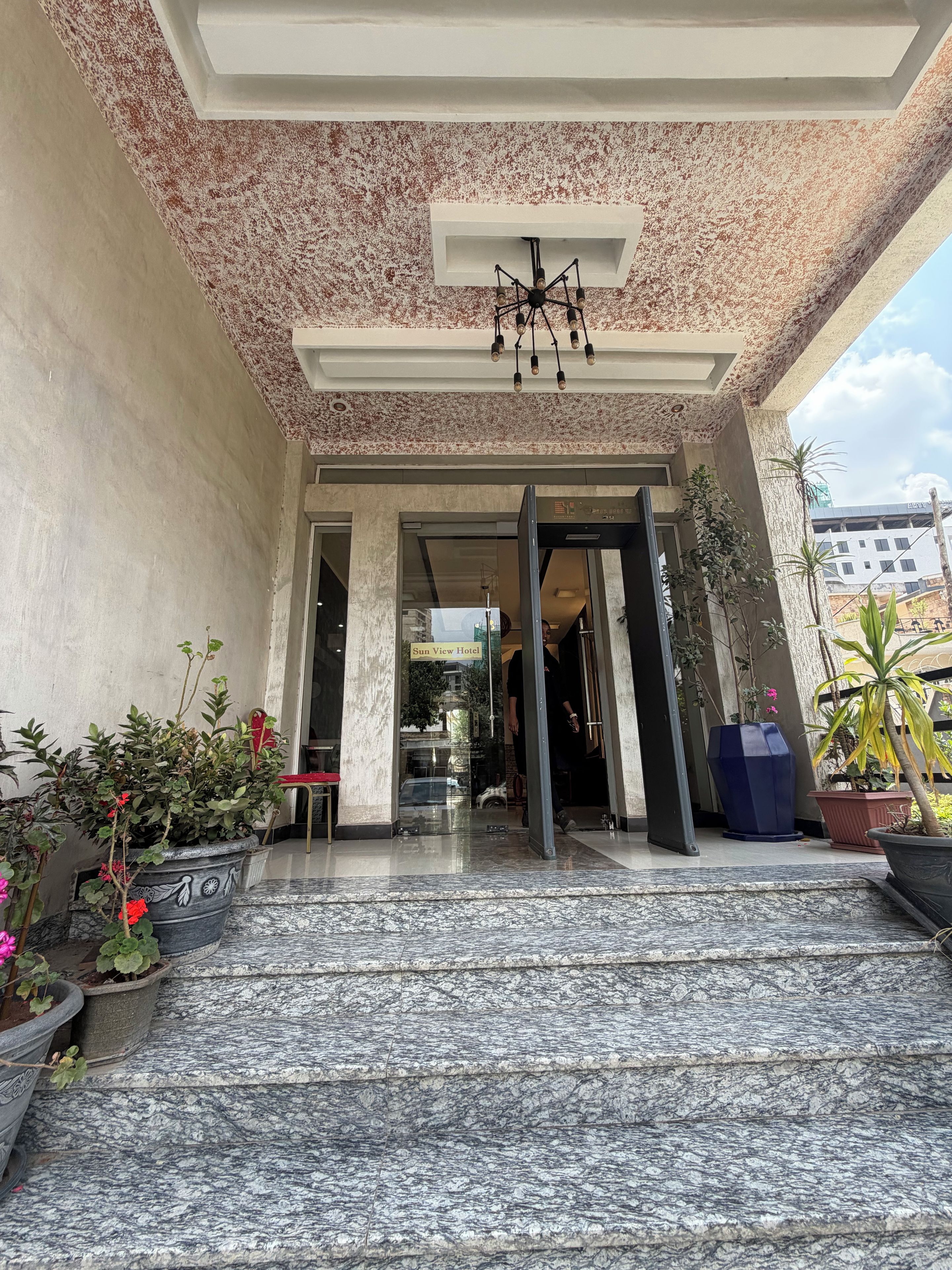 Entrada de hotel con una escalinata de mármol, un candelabro y plantas en macetas.