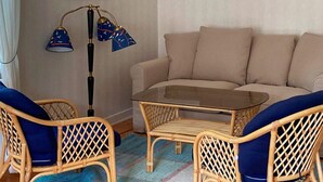 A living room with a beige sofa, two wicker chairs with blue cushions, a glass coffee table, and a floor lamp with three lampshades. - 6 Person Holiday Home in Dalskog (Dalskog)