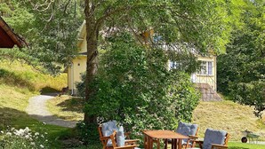 A patio with wooden furniture and a small table, surrounded by greenery and a path leading to a building. - 6 Person Holiday Home in Dalskog (Dalskog)