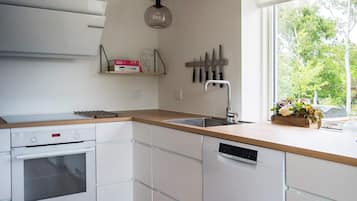 A modern kitchen with white cabinetry, a built-in oven, a dishwasher, and a window providing a view of trees.