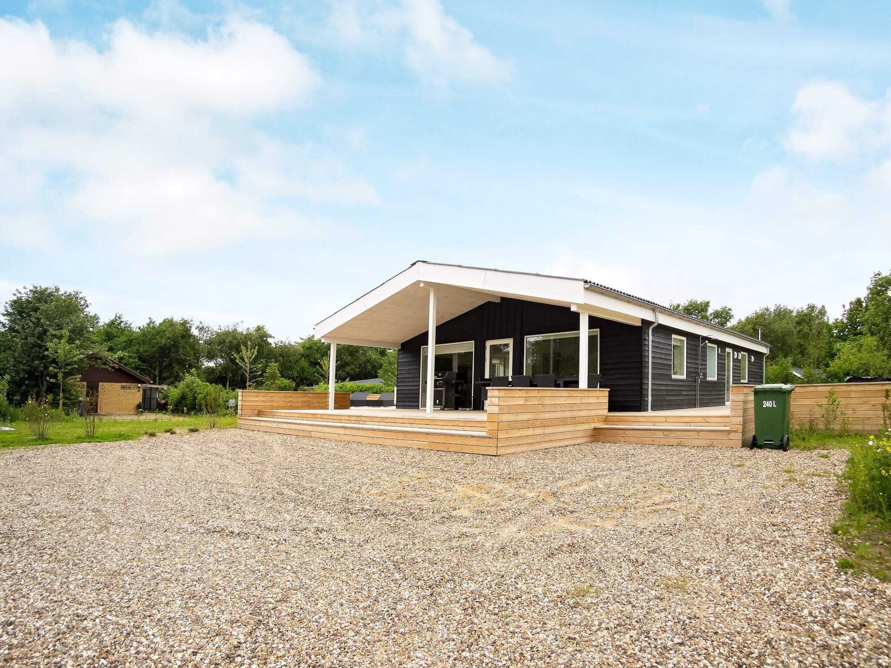 A modern house with a covered porch, a gravel driveway, and a green trash bin.