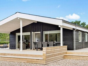 Una casa moderna con un porche cubierto, ventanas amplias y una terraza de madera.