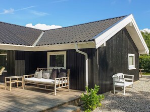 Eine Holzterrasse mit einer Couch, Stühlen, einem kleinen Tisch und einem Fenster.