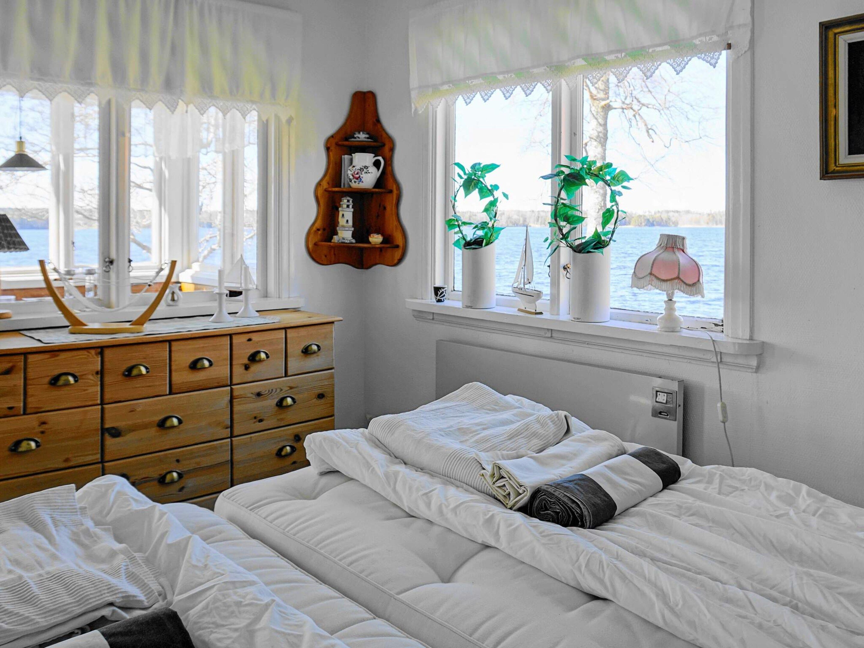 Un dormitorio con cama, cómoda, ventanas con cortinas y vista al agua.