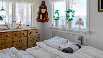 Un dormitorio con cama, cómoda, ventanas con cortinas y vista al agua.