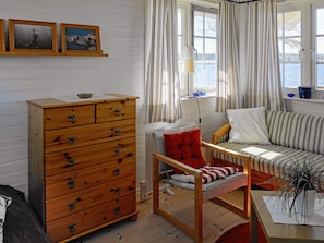 A cozy room with a wooden dresser, a sofa, a chair, and a window with curtains.