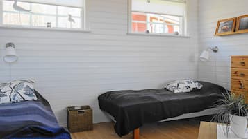 A bedroom with two beds, a wooden dresser, a small plant, and two windows with views of the outside.