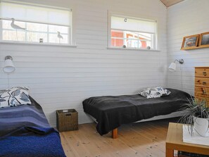 A bedroom with two beds, a wooden dresser, a small plant, and two windows with views of the outside.